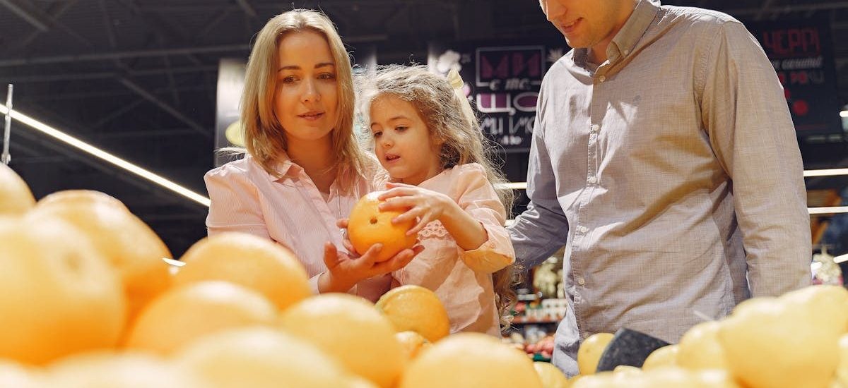 Parents and child selecting fresh oranges together at the supermarket. Captures family bonding and healthy shopping.