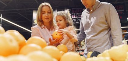 Parents and child selecting fresh oranges together at the supermarket. Captures family bonding and healthy shopping.