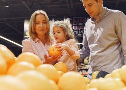 Parents and child selecting fresh oranges together at the supermarket. Captures family bonding and healthy shopping.