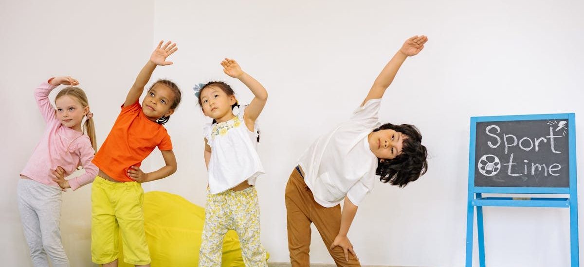 Joyful children stretching during indoor sport time in a classroom.