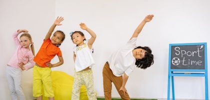 Joyful children stretching during indoor sport time in a classroom.