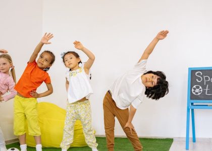 Joyful children stretching during indoor sport time in a classroom.